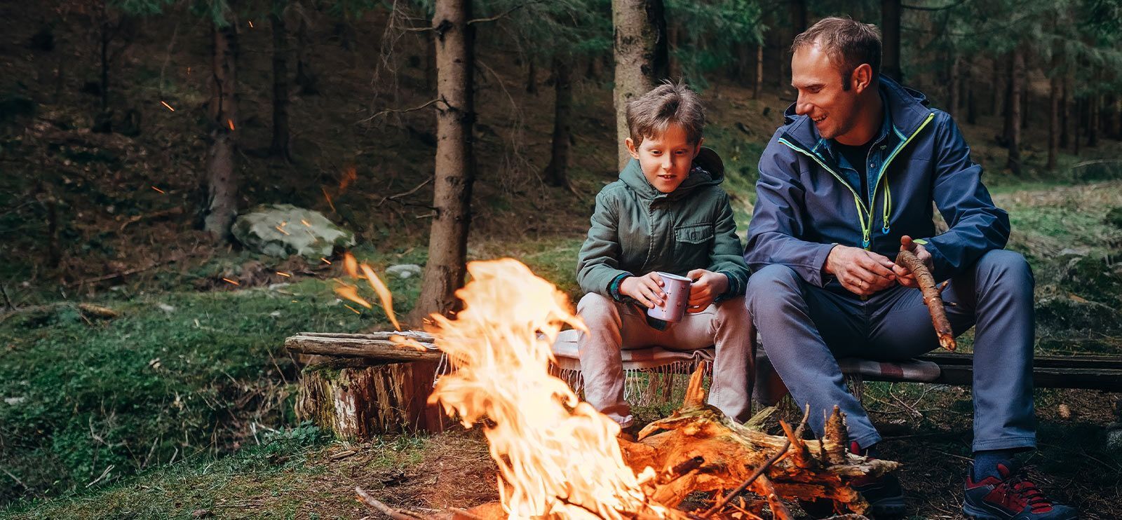 Far og sønn som brenner bål i skogen.
