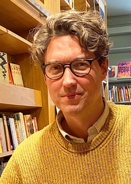 Bokhandler med gul genser, krøllete brunt hår og briller.